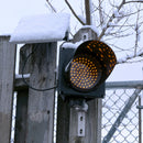 Amber solar powered 8 inch traffic light mounted outdoors with recent snowfall.